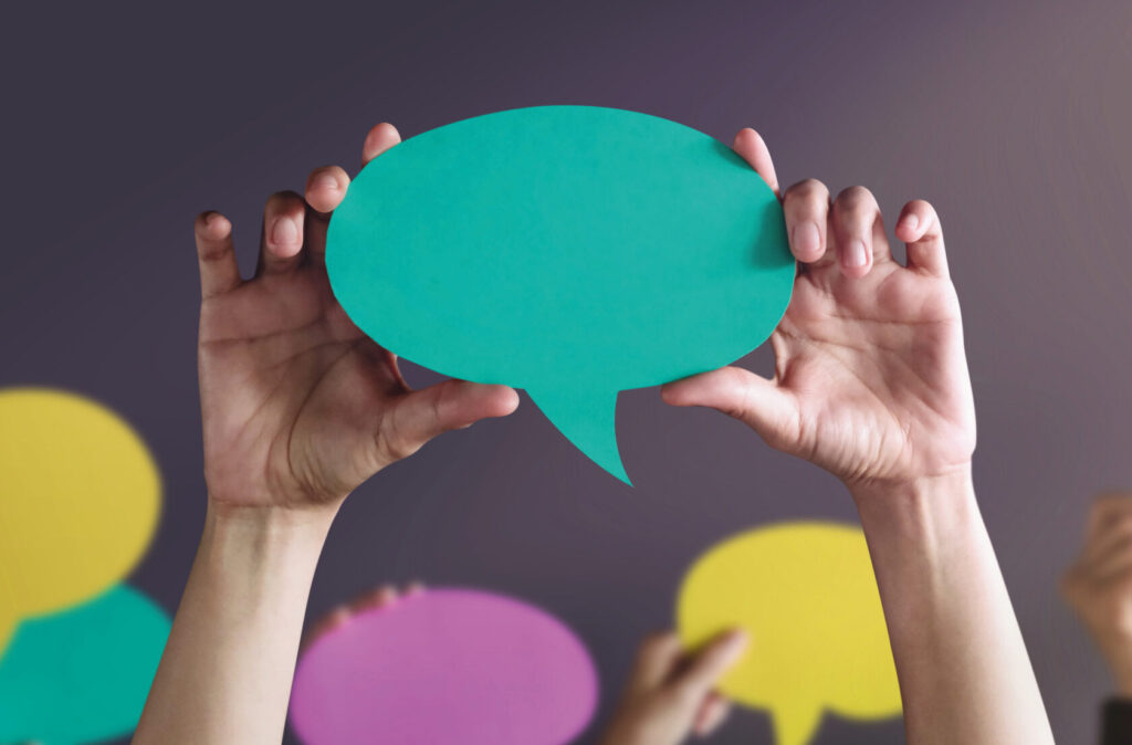 Manos sosteniendo carteles de colores en forma de burbujas de diálogo.