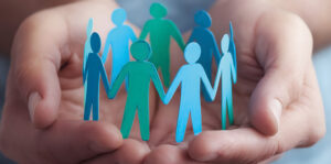 Manos sosteniendo figuras de papel en colores variados que representan personas.