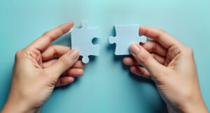Dos manos sosteniendo piezas de rompecabezas blancas sobre fondo azul.