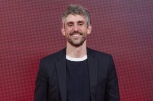 Hombre sonriente con cabello rizado y chaqueta negra