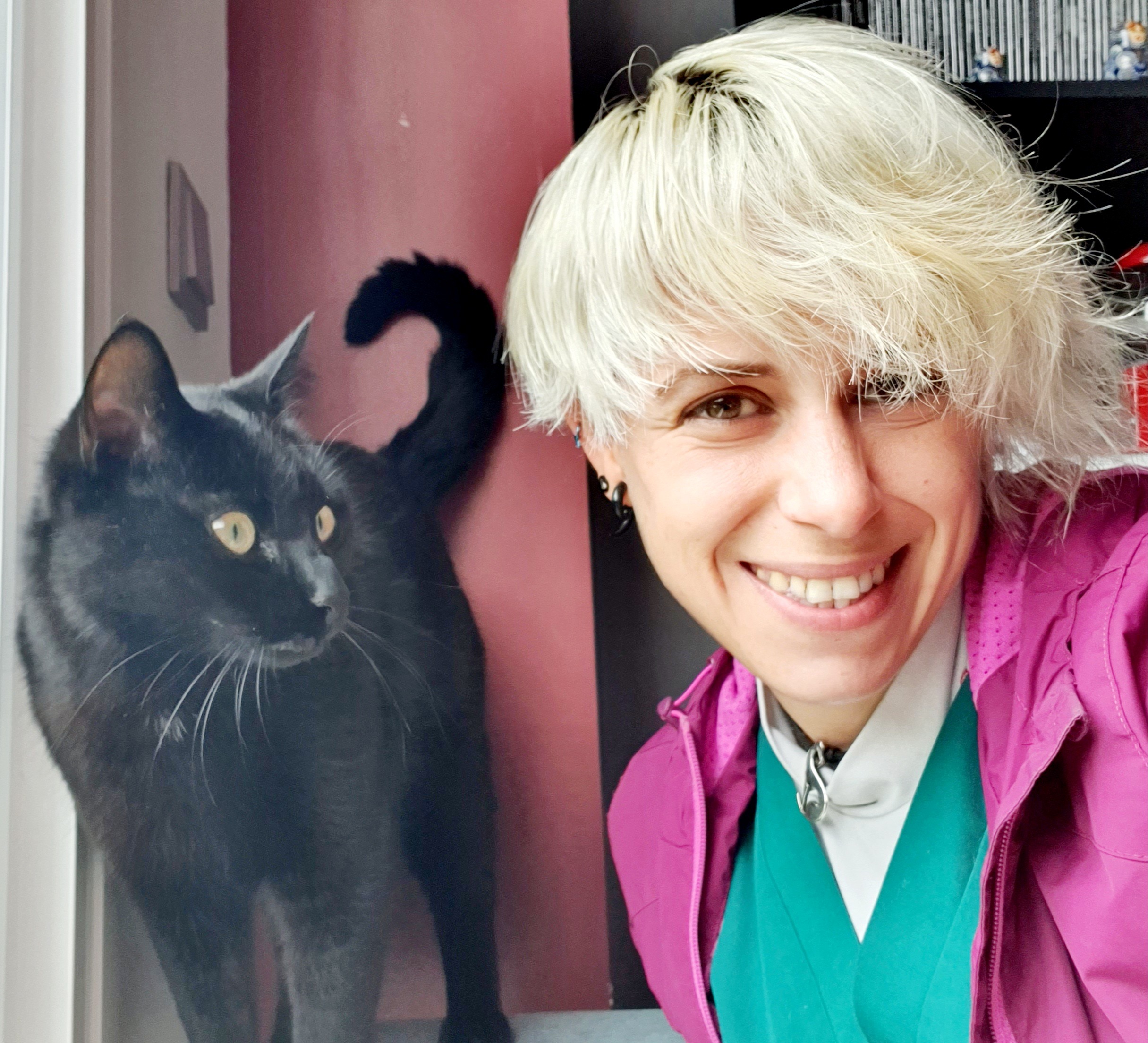 Persona sonriente con cabello rubio y gato negro al lado
